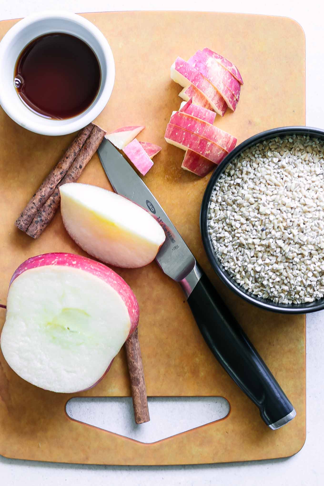 sliced apples on a cutting board with cinnamon sticks and a bowl of dry oatmeal