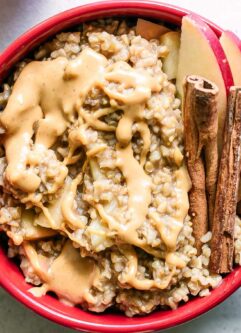 a bowl of oatmeal with apple slices and cinnamon sticks on a white table