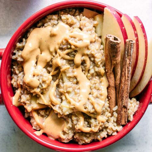 a bowl of oatmeal with apple slices and cinnamon sticks on a white table