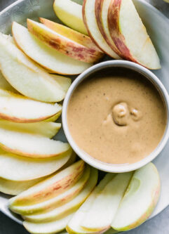 a bowl with peanut butter and apple slices on a white table