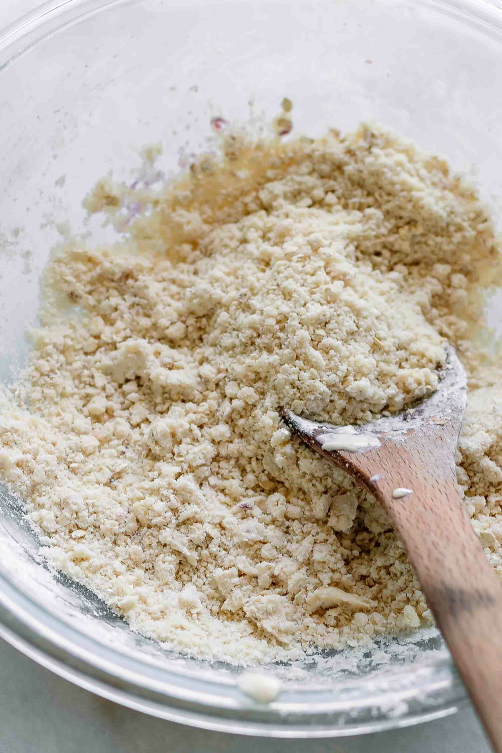 a flour and oat crumble for topping a cherry crisp in a mixing bowl with a wooden spoon
