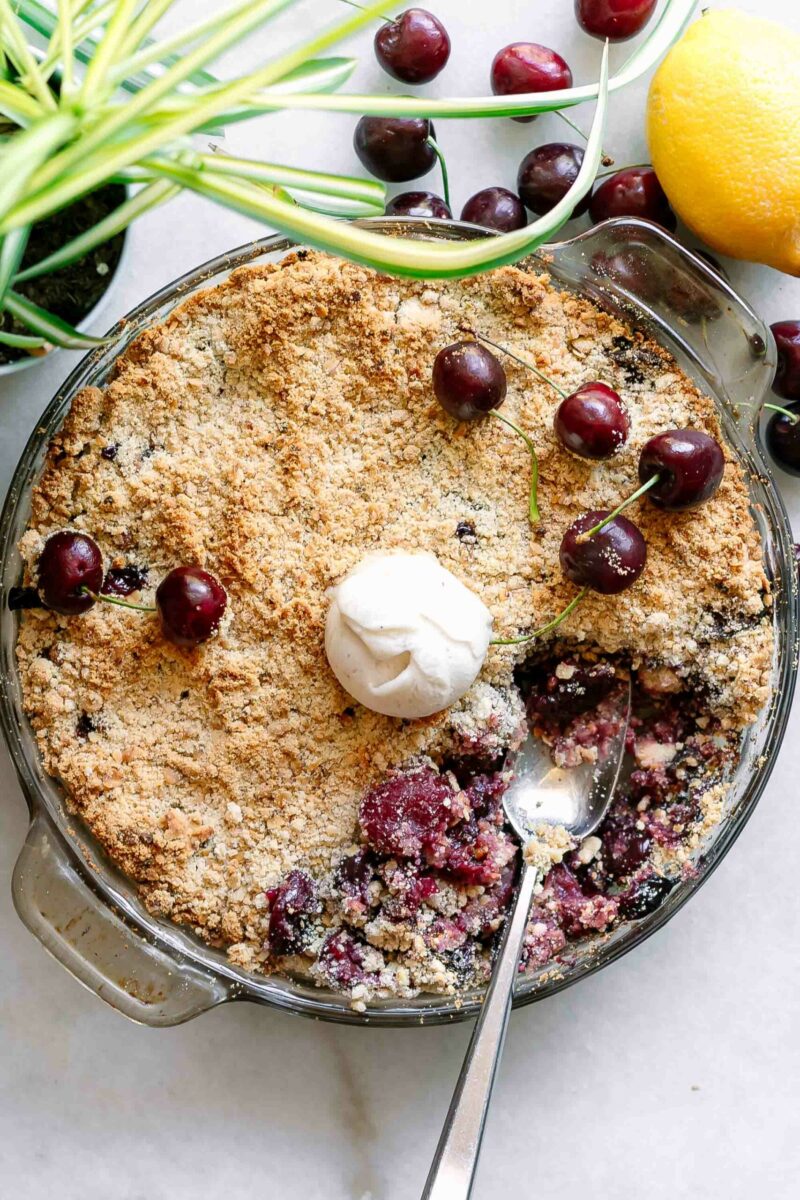 a round baking dish with a baked cherry crisp and a scoop of ice cream on top with a gold fork
