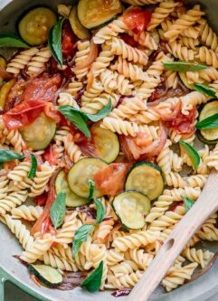 zucchini and tomato pasta with fresh basil in a pan with a spoon after cooking