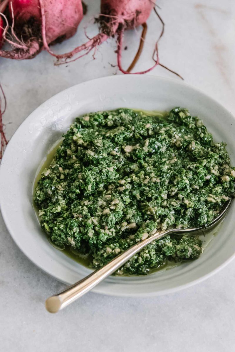 a pesto made with beet leaves in a white bowl with a gold fork and beets in the background