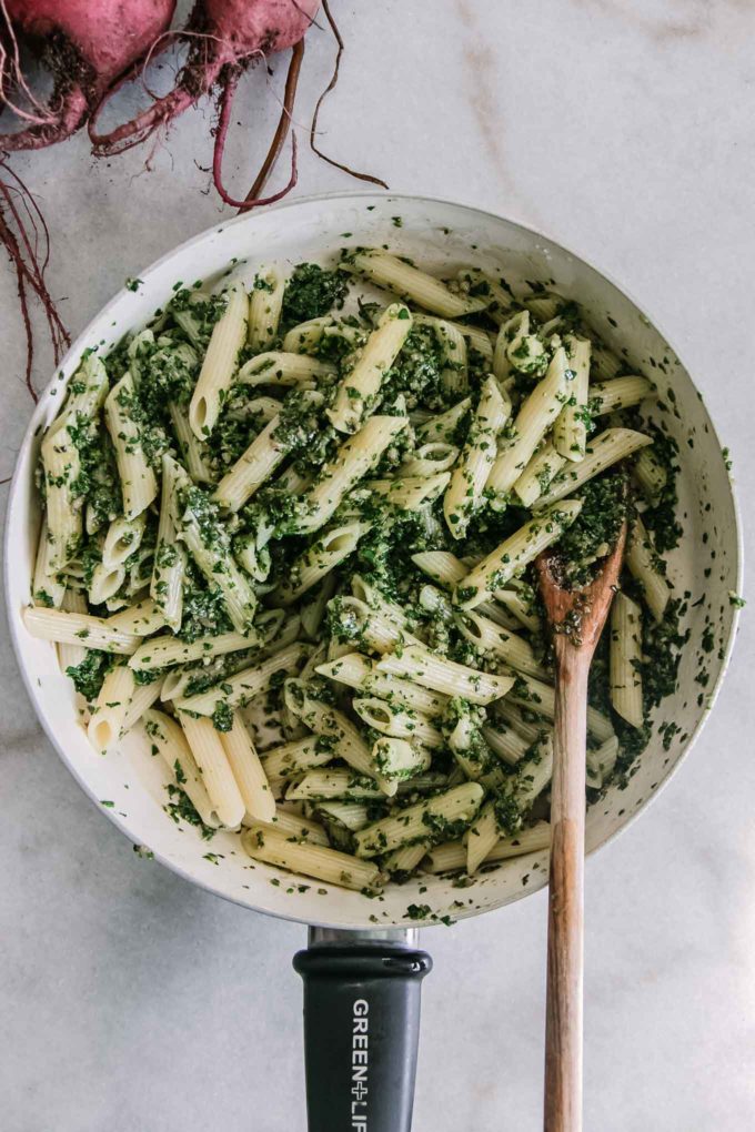 penne noodles in a pan with pesto and wooden spoon on a white table