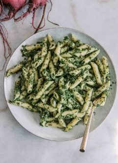 penne pasta noodles with pesto made of beet leaves on a white plate with a gold fork and red beets in the background