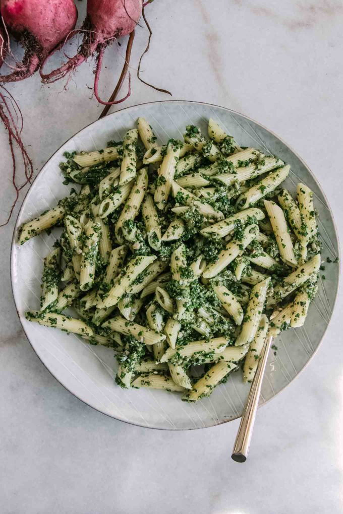 penne pasta noodles with pesto made of beet leaves on a white plate with a gold fork and red beets in the background