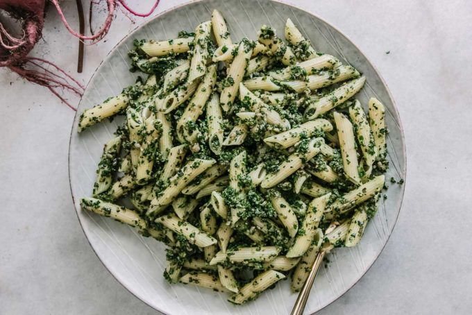 beet leaves pesto pasta on a blue plate on a white table