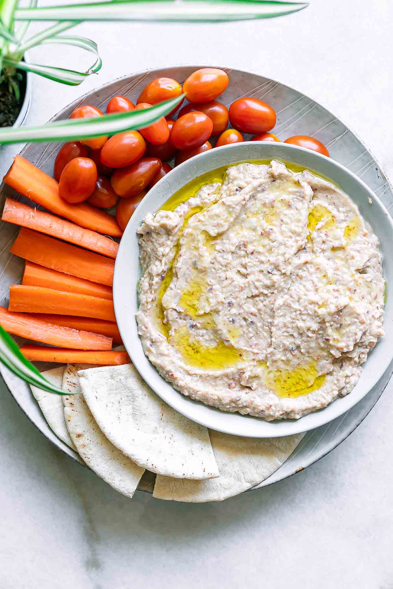 hummus made with black eyed peas in a bowl with a plate of vegetables and pita bread for dipping