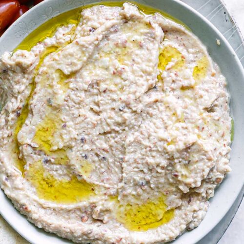 a bowl of black eyed pea hummus on a plate with cherry tomatoes, carrot sticks, and pita bread