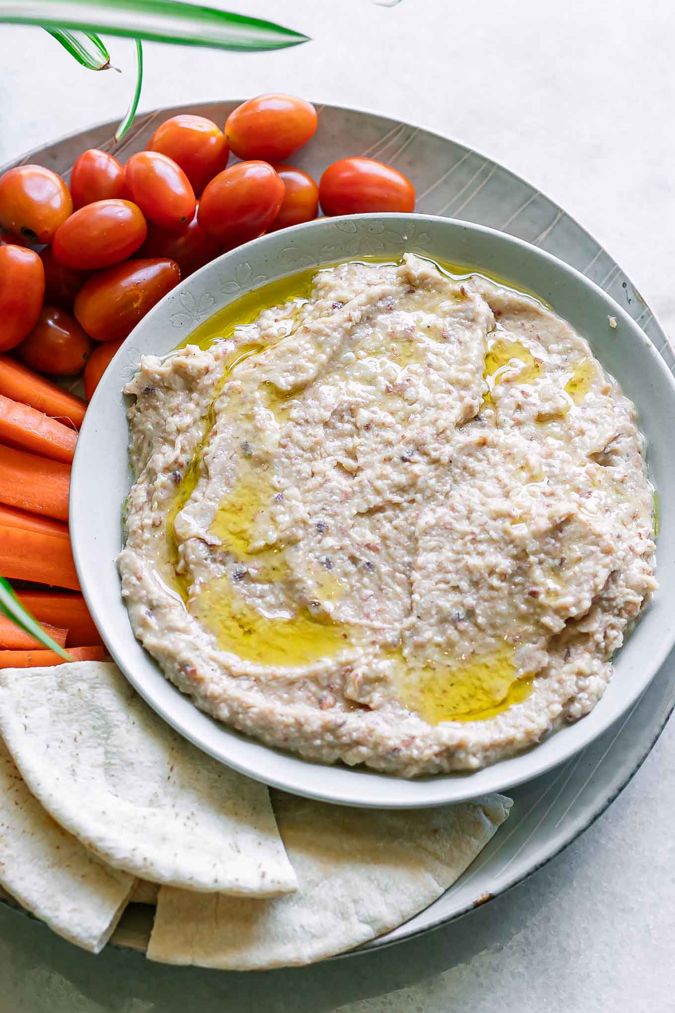 a close up photo of a board with a bowl of black eyed pea hummus on a plate with cut vegetables for dipping