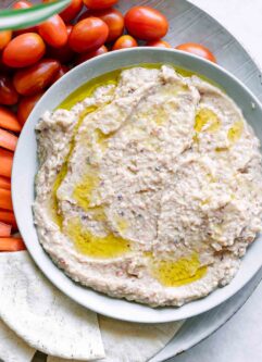 a bowl of black eyed pea hummus with pita bread, carrot sticks, and cherry tomatoes on a white table