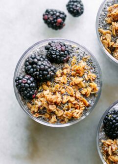 a top down photo of the top of three glasses of blackberry chia pudding with granola and fresh blackberries as garnish