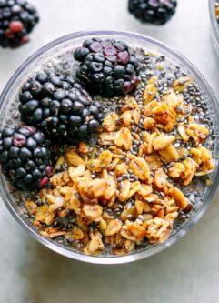 a close up photo of a glass of blackberry-flavored chia seed pudding with granola and fresh blackberries as garnish