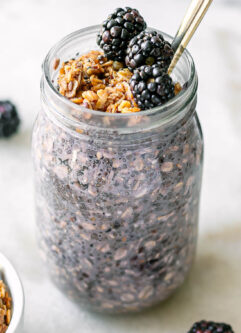a jar of blackberry chia seed pudding with granola and fresh blackberries on a white table