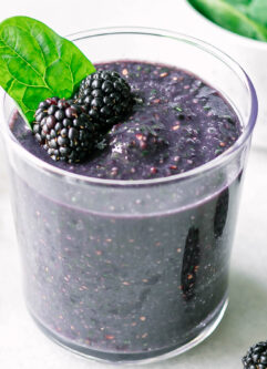 a spinach blackberry smoothie in a glass on a white table with fresh blackberries