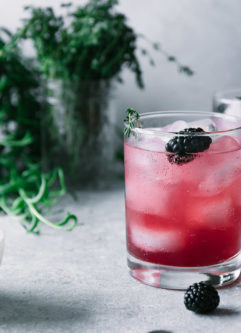 a glass of blackberry-infused sparkling water with fresh thyme in the background