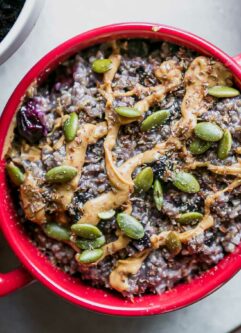 a bowl of blueberry oatmeal with drizzled nut butter and seeds on top