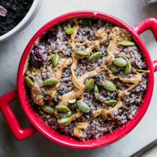 a bowl of blueberry oatmeal with drizzled nut butter and seeds on top
