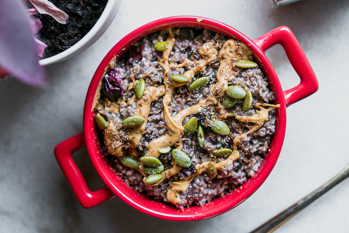a bowl of blueberry oatmeal with drizzled nut butter and seeds on top