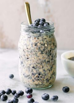 blueberry overnight oats in a mason jar on a white table with a gold spoon