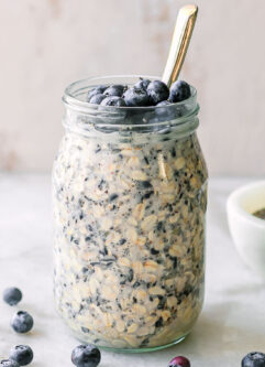 a jar of blueberry overnight oats with fresh blueberry garnish on a white table with a gold spoon