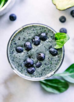 a close up photo of the top of a blueberry spinach smoothie garnished with a spinach leaf and fresh blueberries