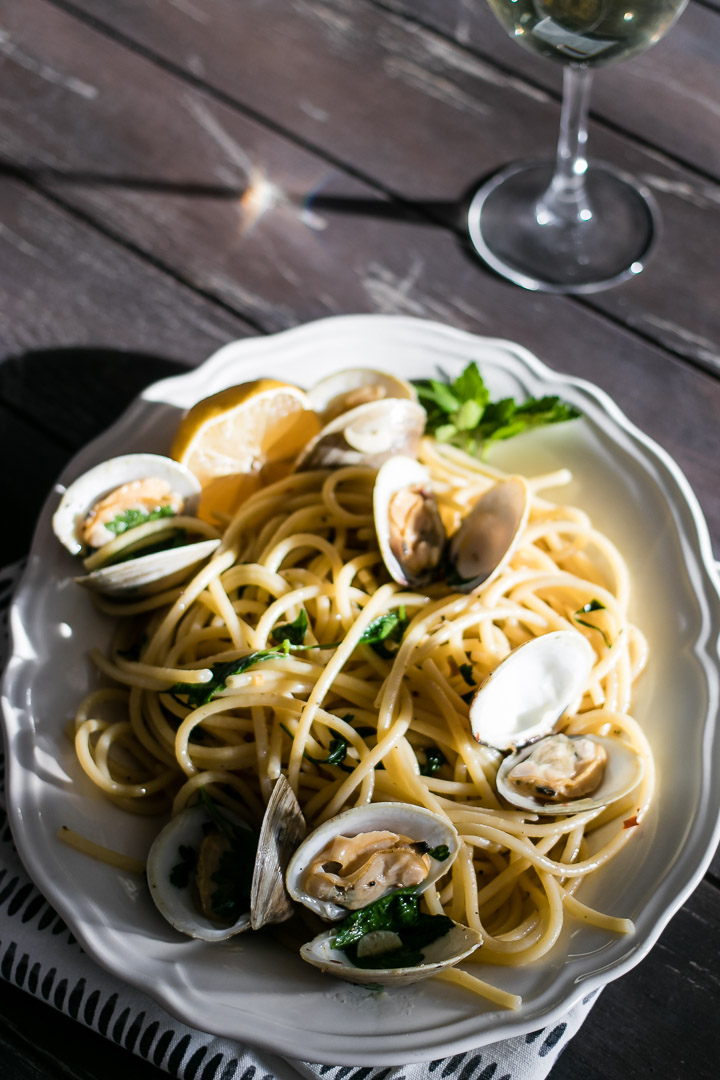 a plate of pasta with clams with a glass of white wine on a wood table