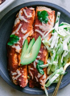 a blue plate with two butternut squash black bean enchiladas with avocado garnish on a white table