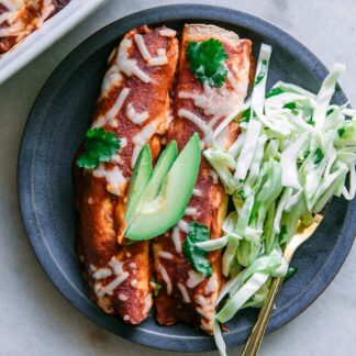 a blue plate with two butternut squash black bean enchiladas with avocado garnish on a white table