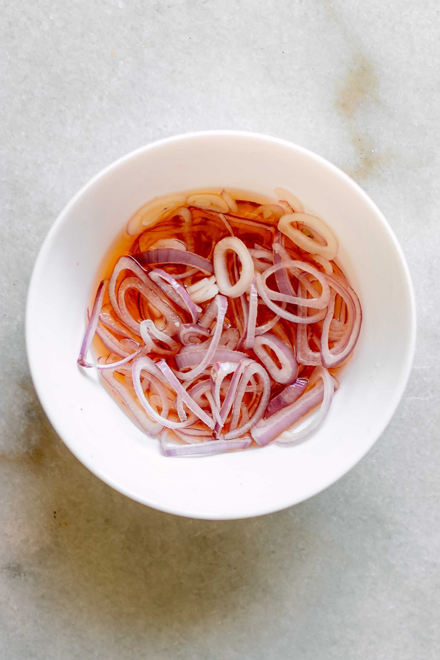 sliced shallots in a bowl of apple cider vinegar on a white table