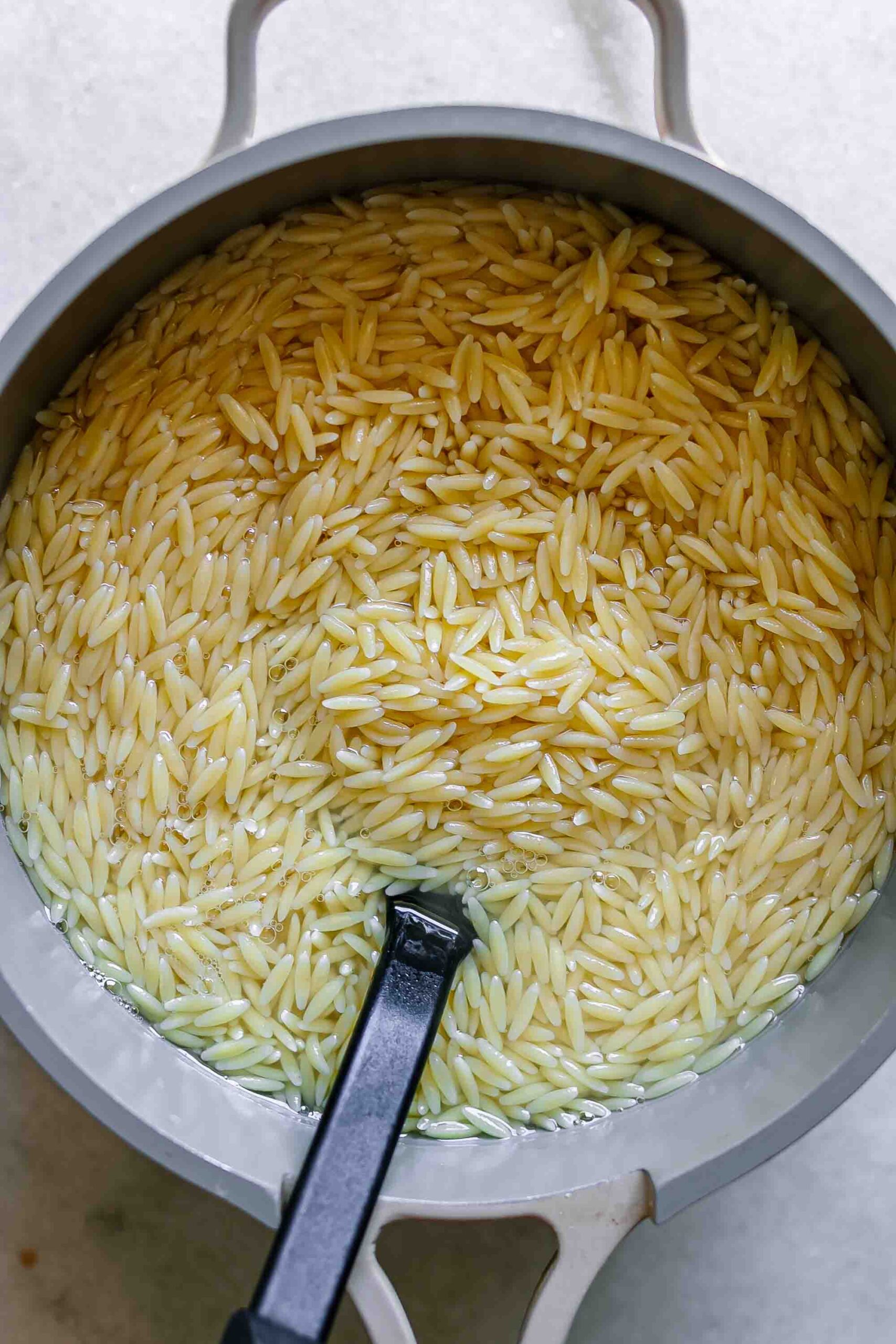 a pot of cooked orzo with a black spoon