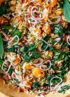 a large salad bowl with orzo butternut squash and kale salad on a white table