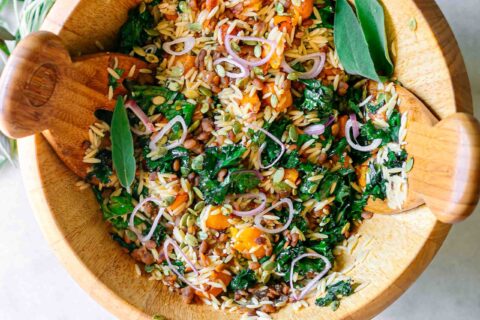 a large salad bowl with orzo butternut squash and kale salad on a white table