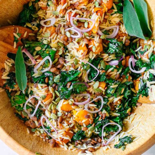 a large salad bowl with orzo butternut squash and kale salad on a white table
