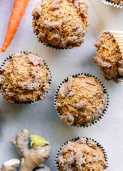 vegan carrot cake muffins on a white table with carrots and fresh ginger