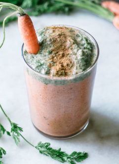 an orange carrot smoothie with a green carrot tops smoothie layer on top in a glass on a white table