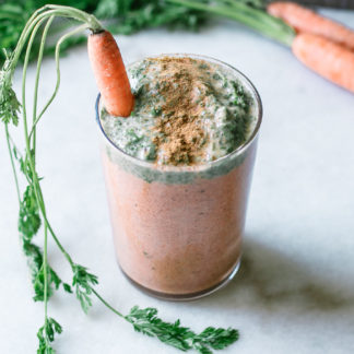 an orange carrot smoothie with a green carrot tops smoothie layer on top in a glass on a white table