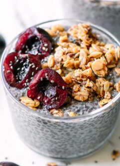 a bowl of cherry chia seed pudding with cherries and granola garnish on a white table