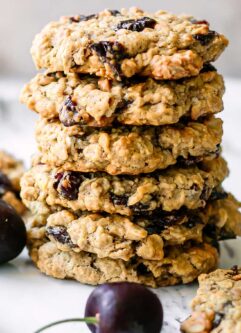 stacked plant-based cherry oatmeal cookies on a white table with fresh black cherries