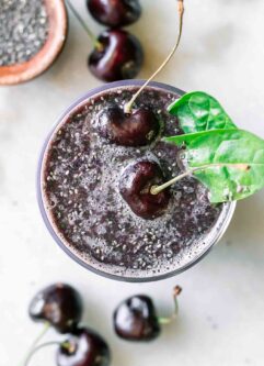 a cherry spinach smoothie with cherries and spinach garnish on a white table