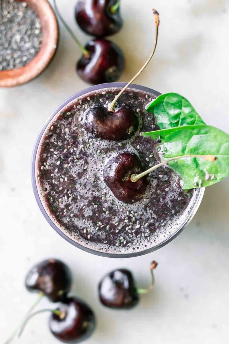 a cherry spinach smoothie with cherries and spinach garnish on a white table
