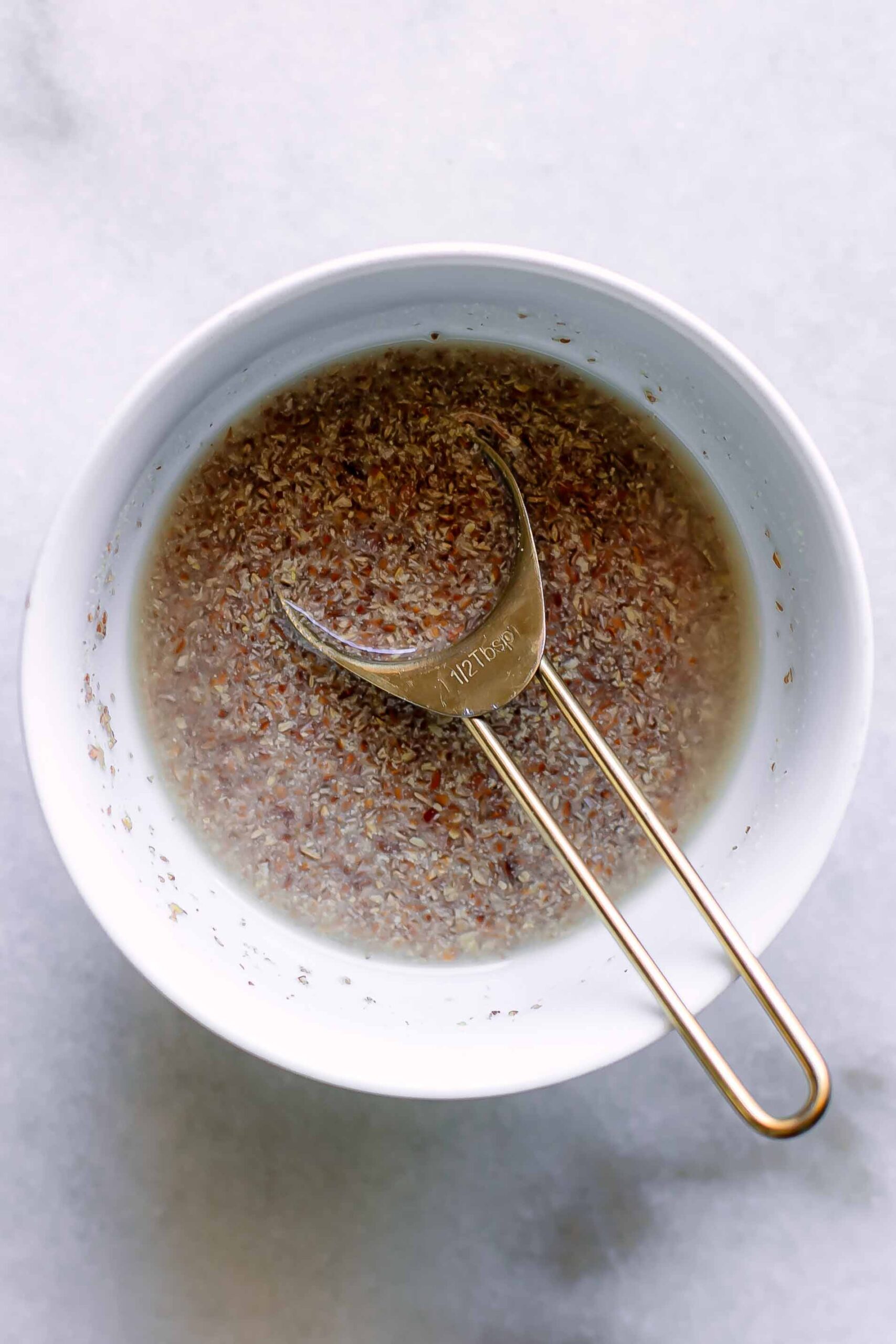 a white bowl with ground flaxseeds and water with a small teaspoon on a white table