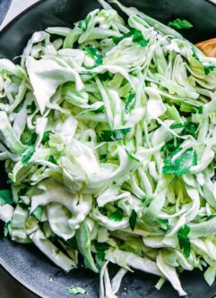 a cabbage cilantro and lime slaw salad in a black bowl on a white table with a lime