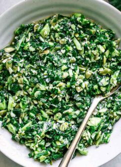a bowl of collard greens pesto sauce on a white table with a gold spoon
