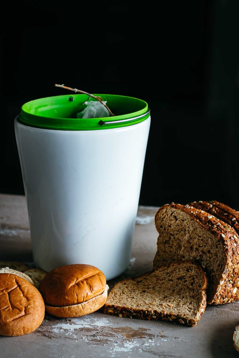 slices of bread and sliced buns next to a compost bin on a countertop