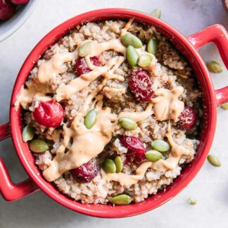 a red bowl of cranberry oatmeal with a gold fork on a white table