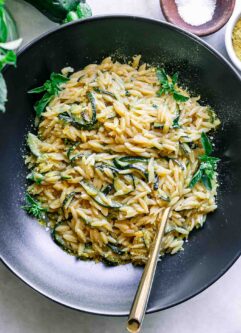 a black bowl with zucchini orzotto pasta with a gold fork on a white table
