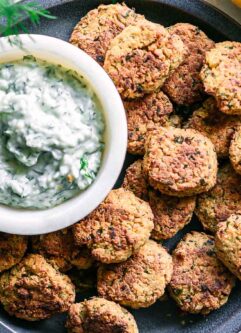 a blue plate with crispy baked falafel balls and a white dipping sauce on a white table