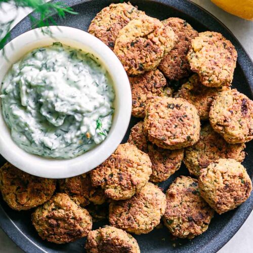 a blue plate with crispy baked falafel balls and a white dipping sauce on a white table
